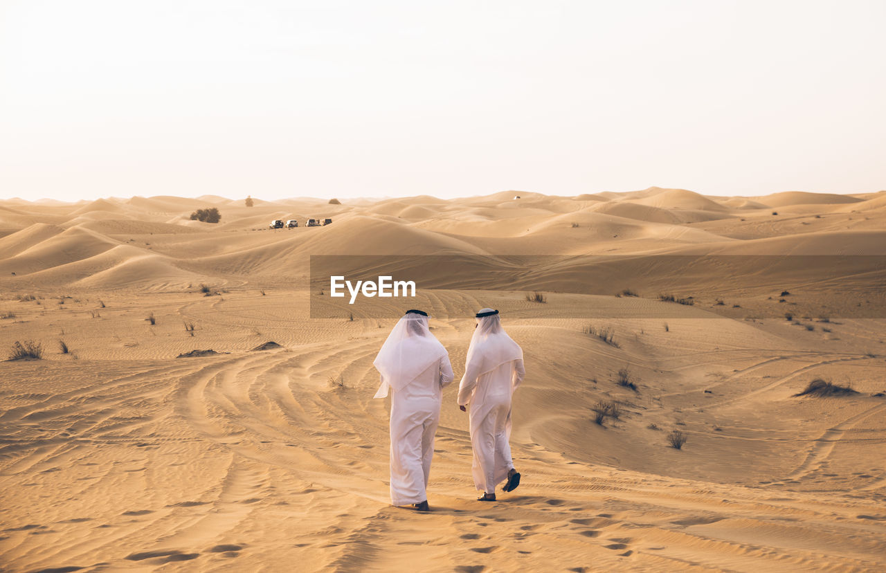 Rear view of men walking in desert against sky