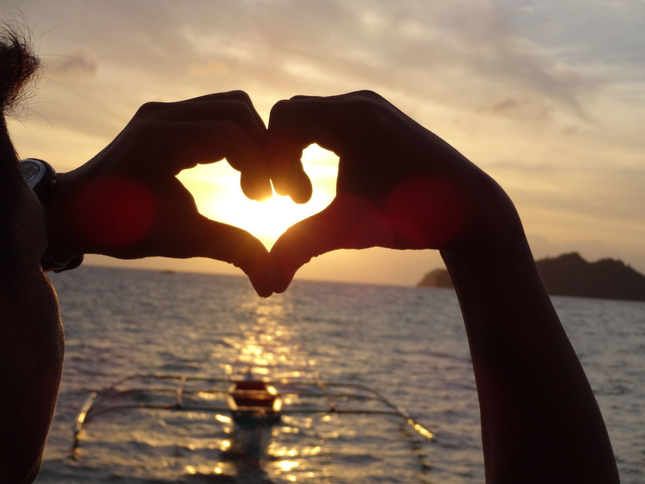 Close-up of hands forming heart shape against sunset
