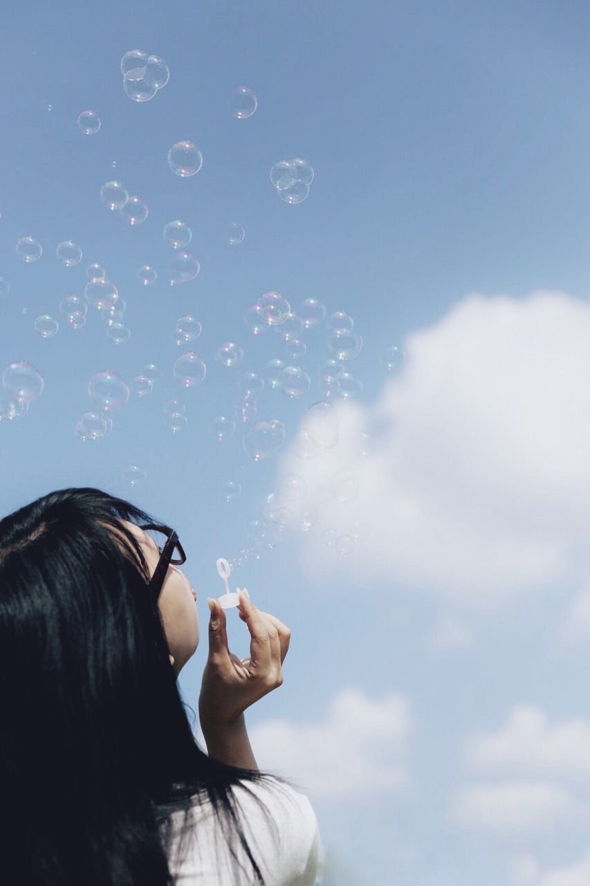 Rear view of woman blowing bubbles against sky