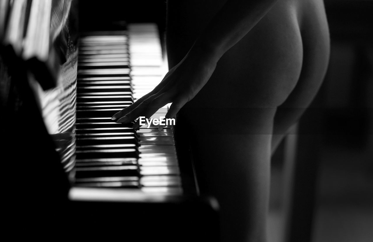 Midsection of naked woman playing piano