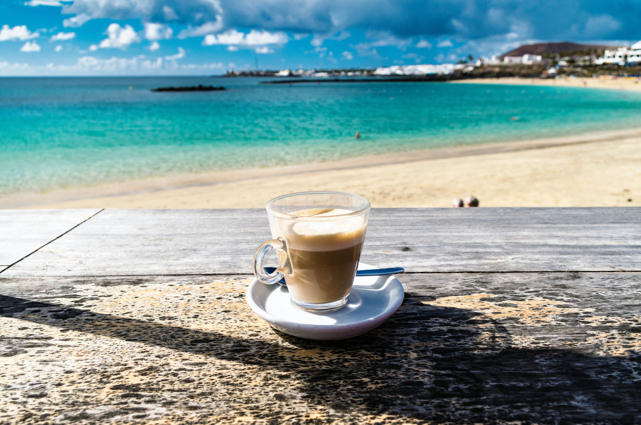 Coffee on table at beach against sky