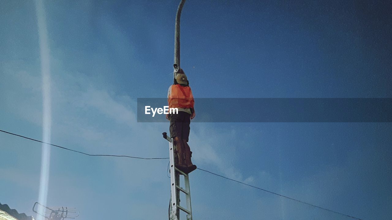 LOW ANGLE VIEW OF MAN WORKING ON POLE AGAINST SKY