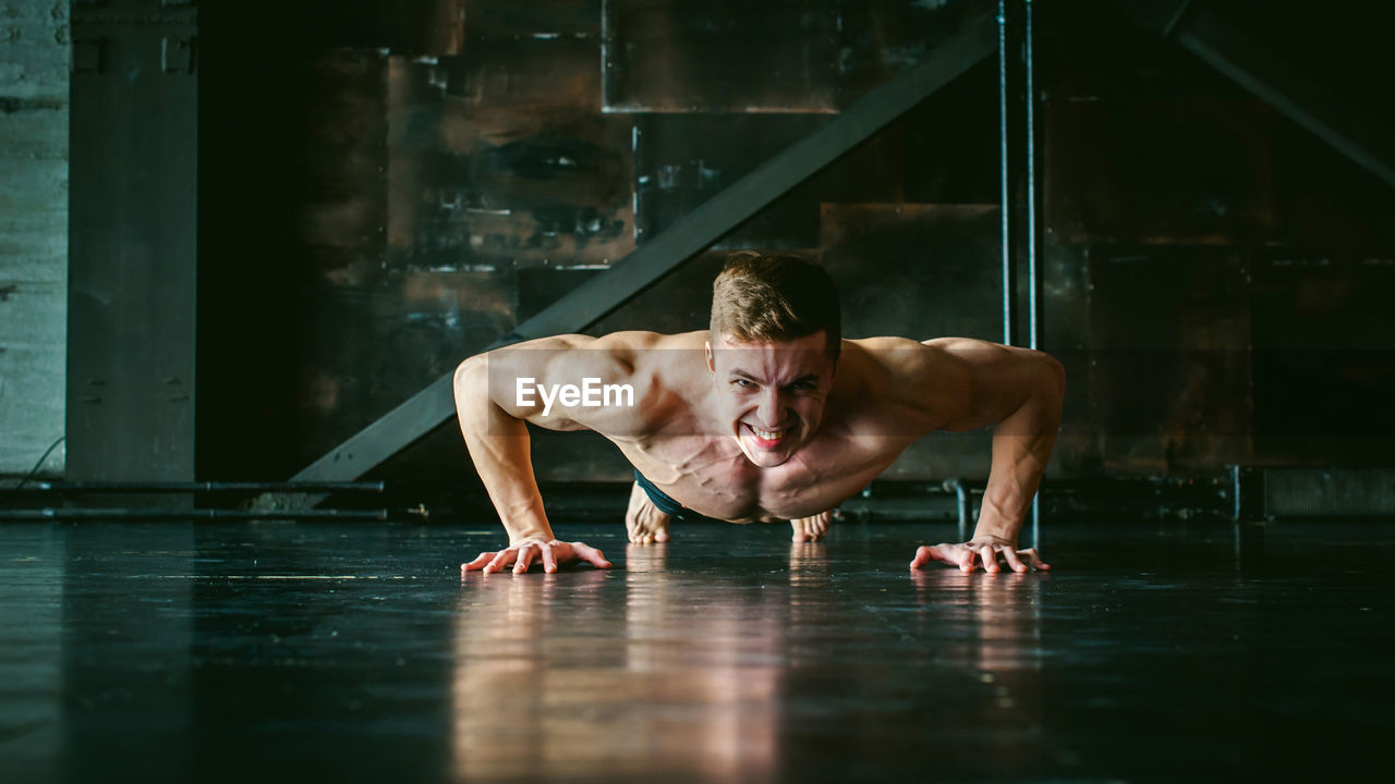 Portrait of shirtless muscular man doing push-ups at home