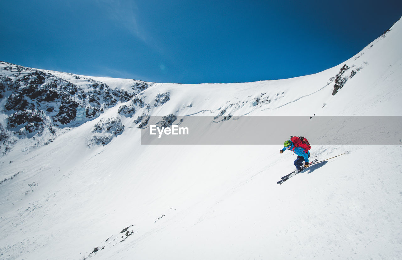PERSON SKIING ON SNOWCAPPED MOUNTAINS AGAINST SKY