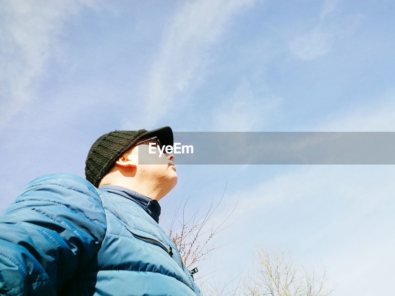 Low angle view of man in hat and sunglasses against sky during sunny day