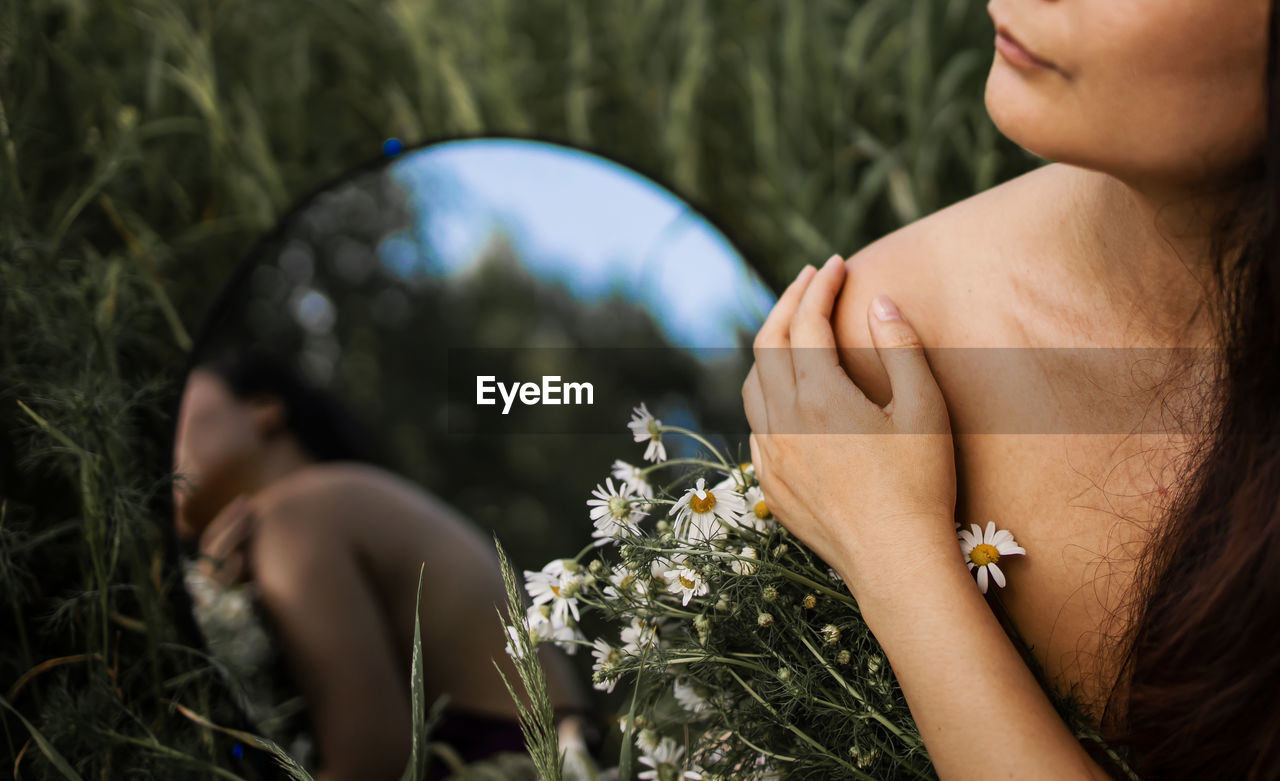 Woman on a green chamomile field with mirror. 