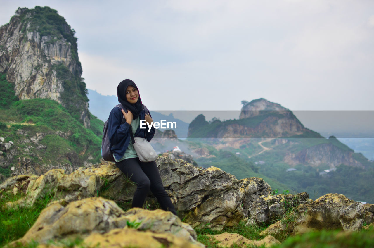 Portrait of woman sitting on rock against mountains