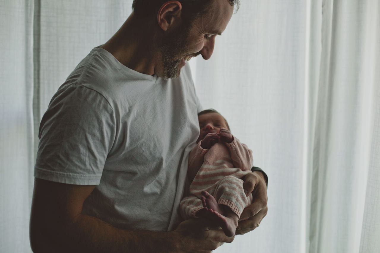 Smiling father carrying baby girl while standing by curtain at home