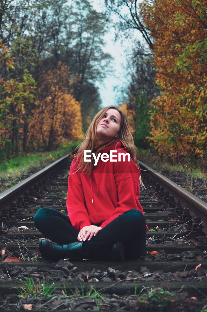 Young woman sitting at railroad track in forest during autumn