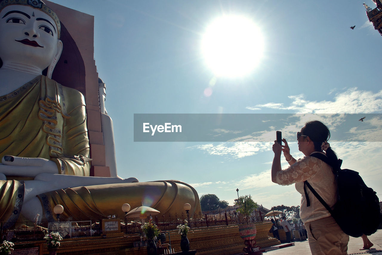 Woman photographing buddha statue against sky 