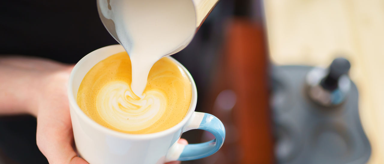 Barista pouring milk into espresso coffee for making cappuccino, latte art