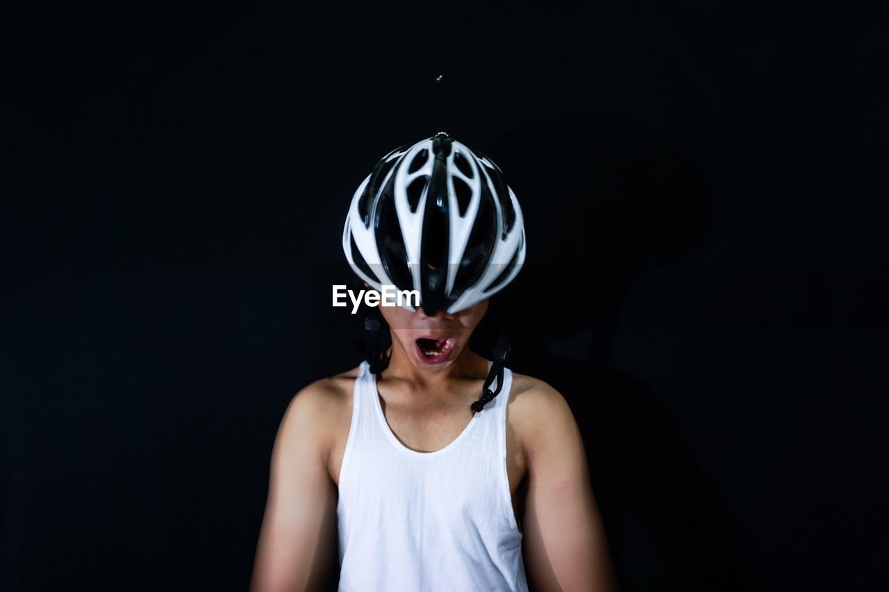 Close-up of man yawning while wearing bicycle helmet against black background