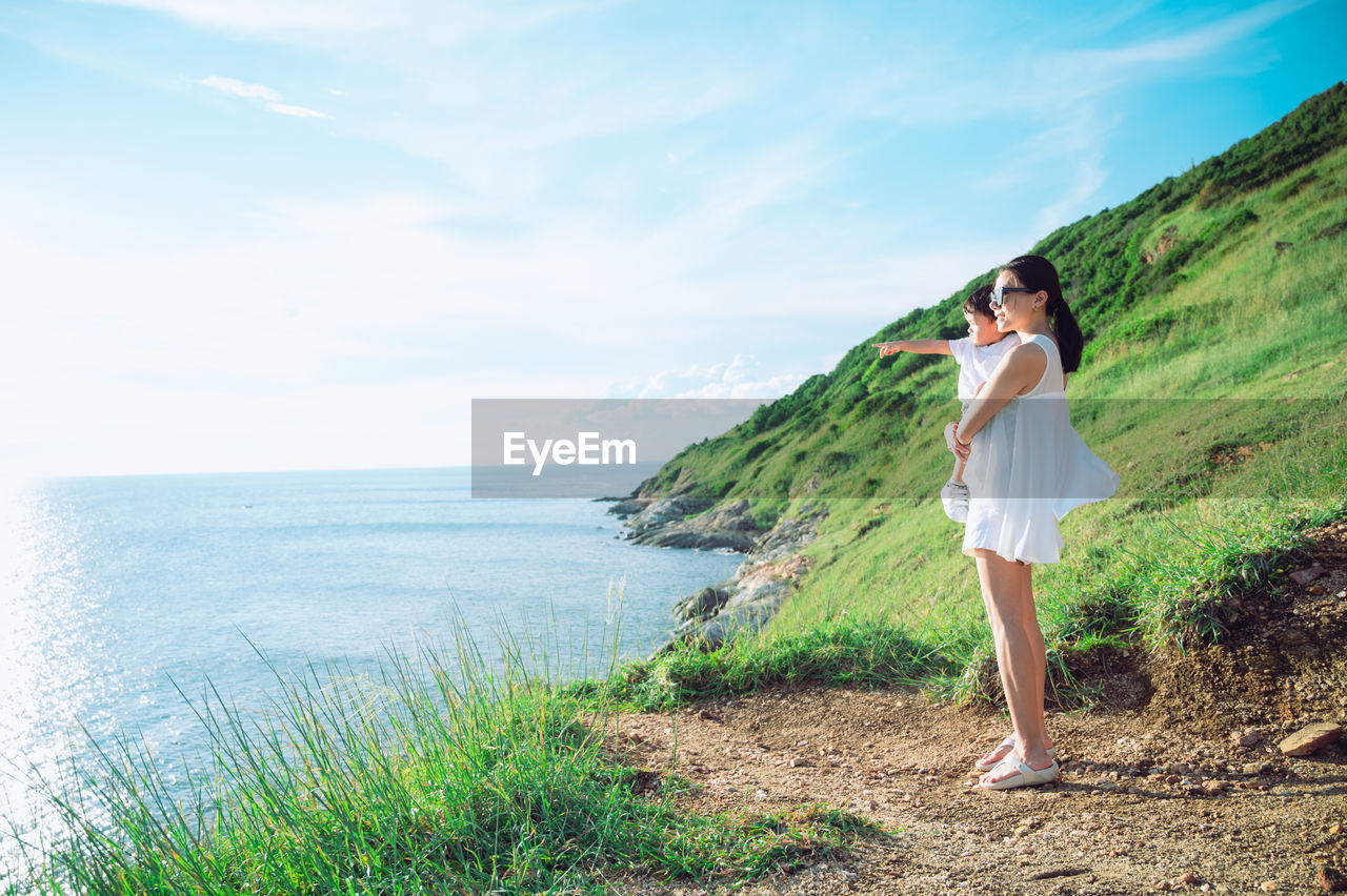 side view of young woman standing against sea against sky