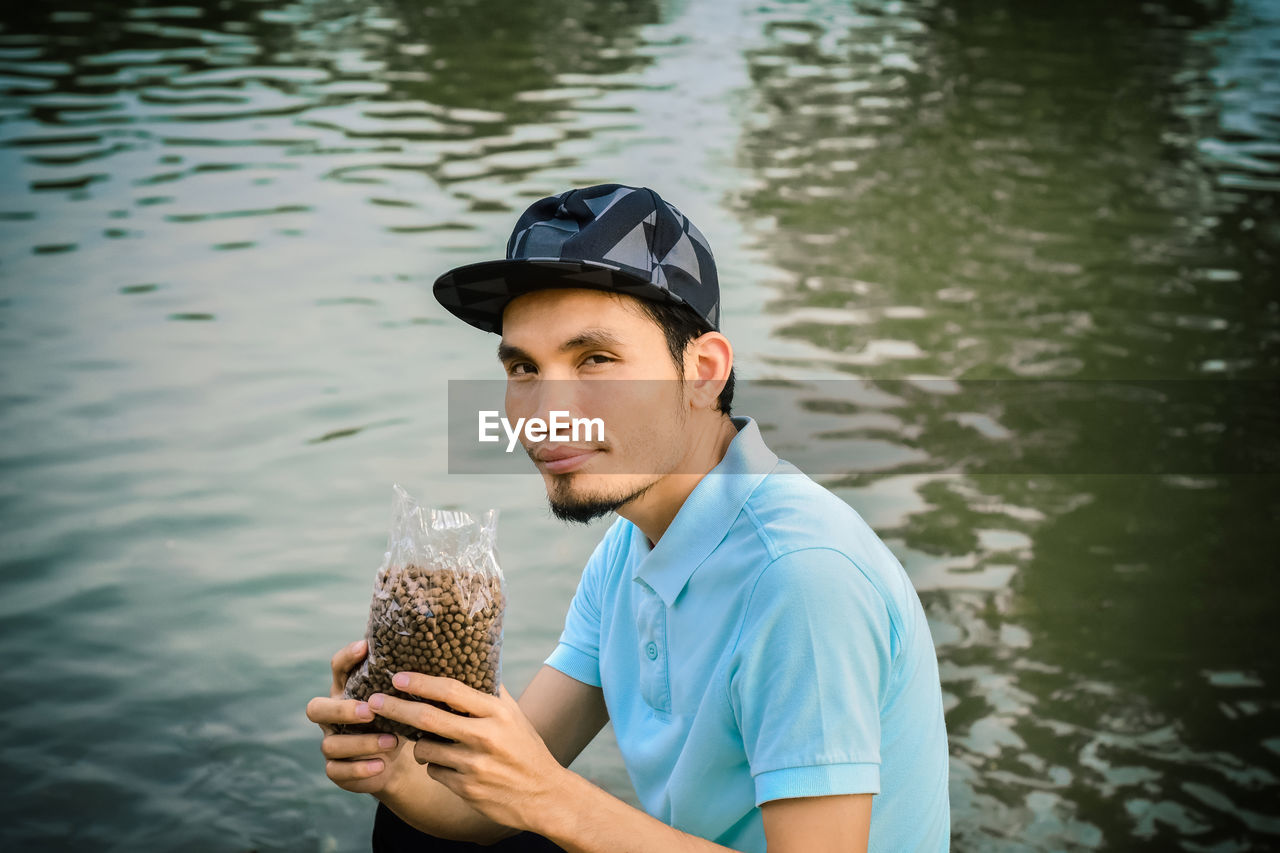 Portrait of man holding seeds in package while sitting against lake