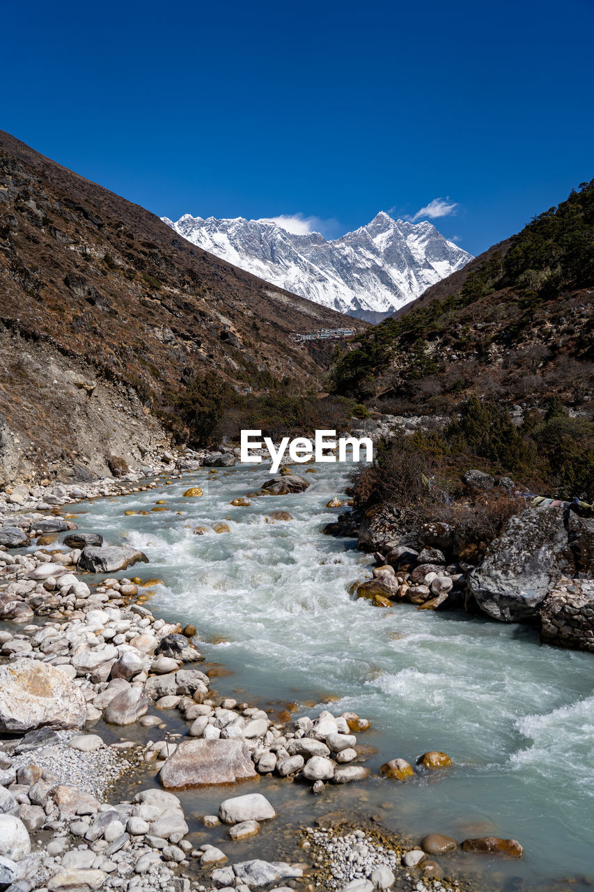 Scenic view of stream amidst snowcapped mountains against sky