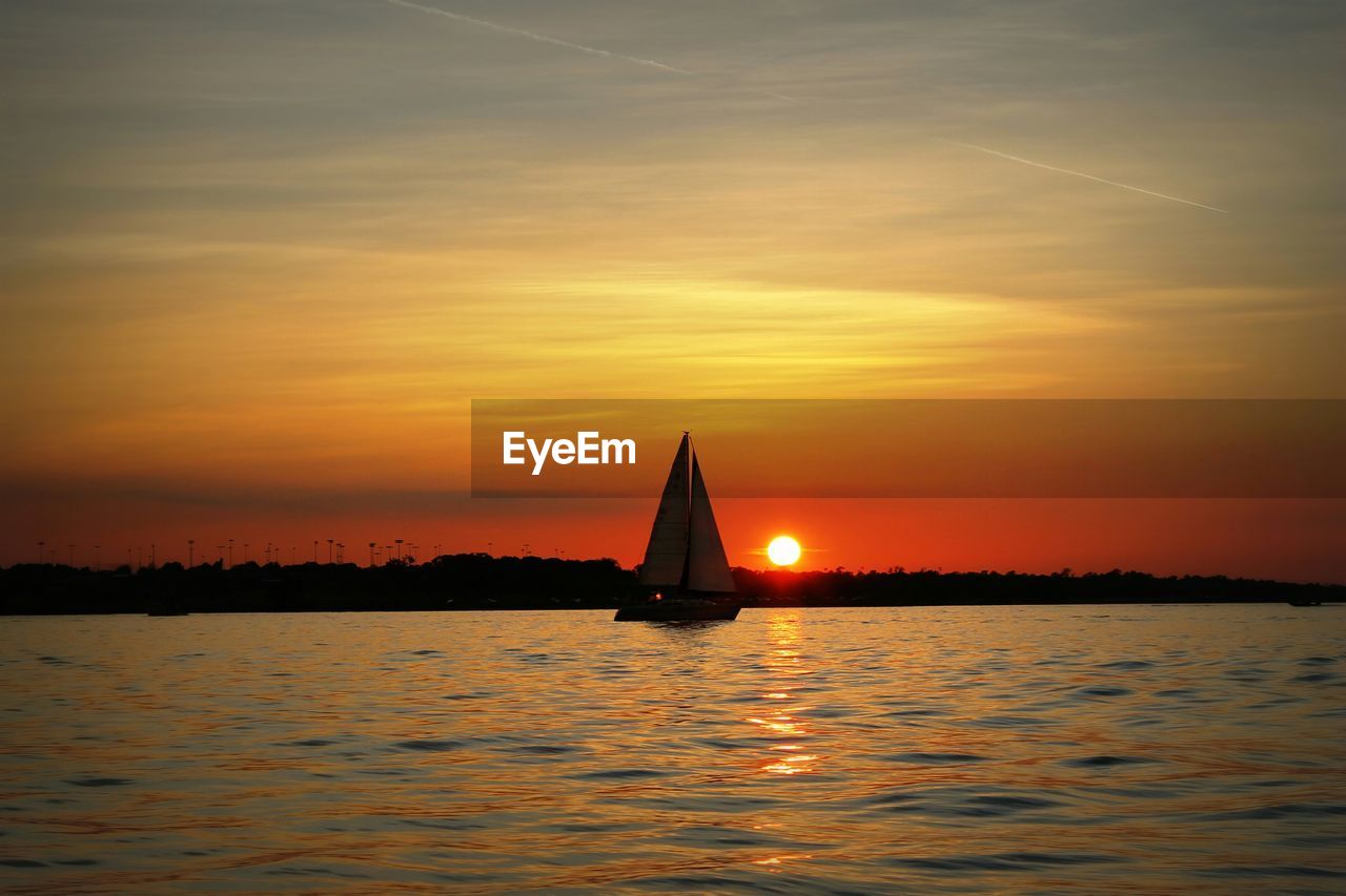 Boat sailing in river against orange sky during sunset
