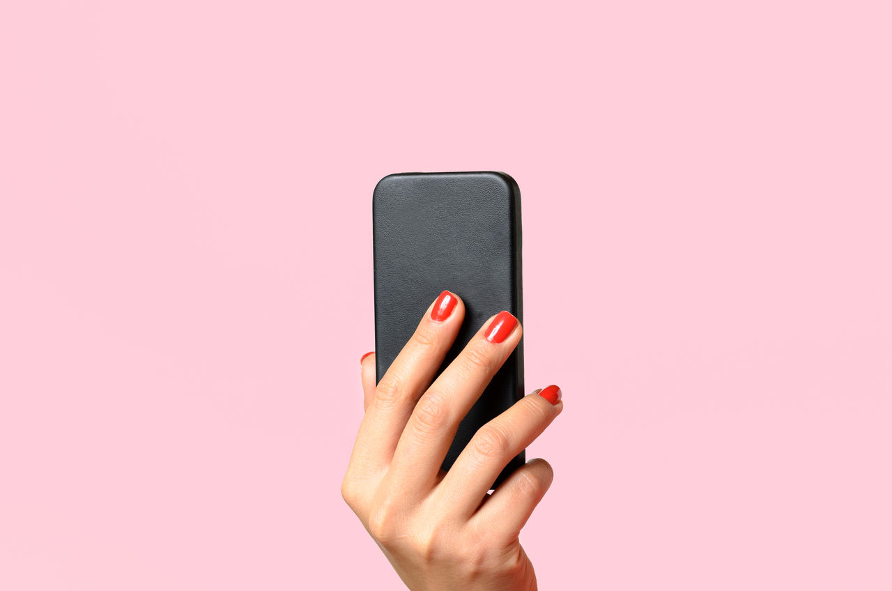 Cropped image of woman hand holding mobile phone against pink background