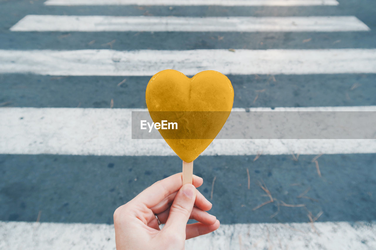 Cropped hand of woman holding heart shape candy on road