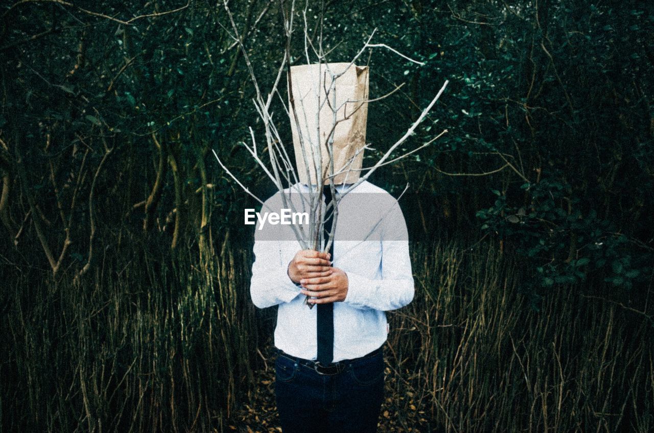 Man in forest holding branches with paper covering face