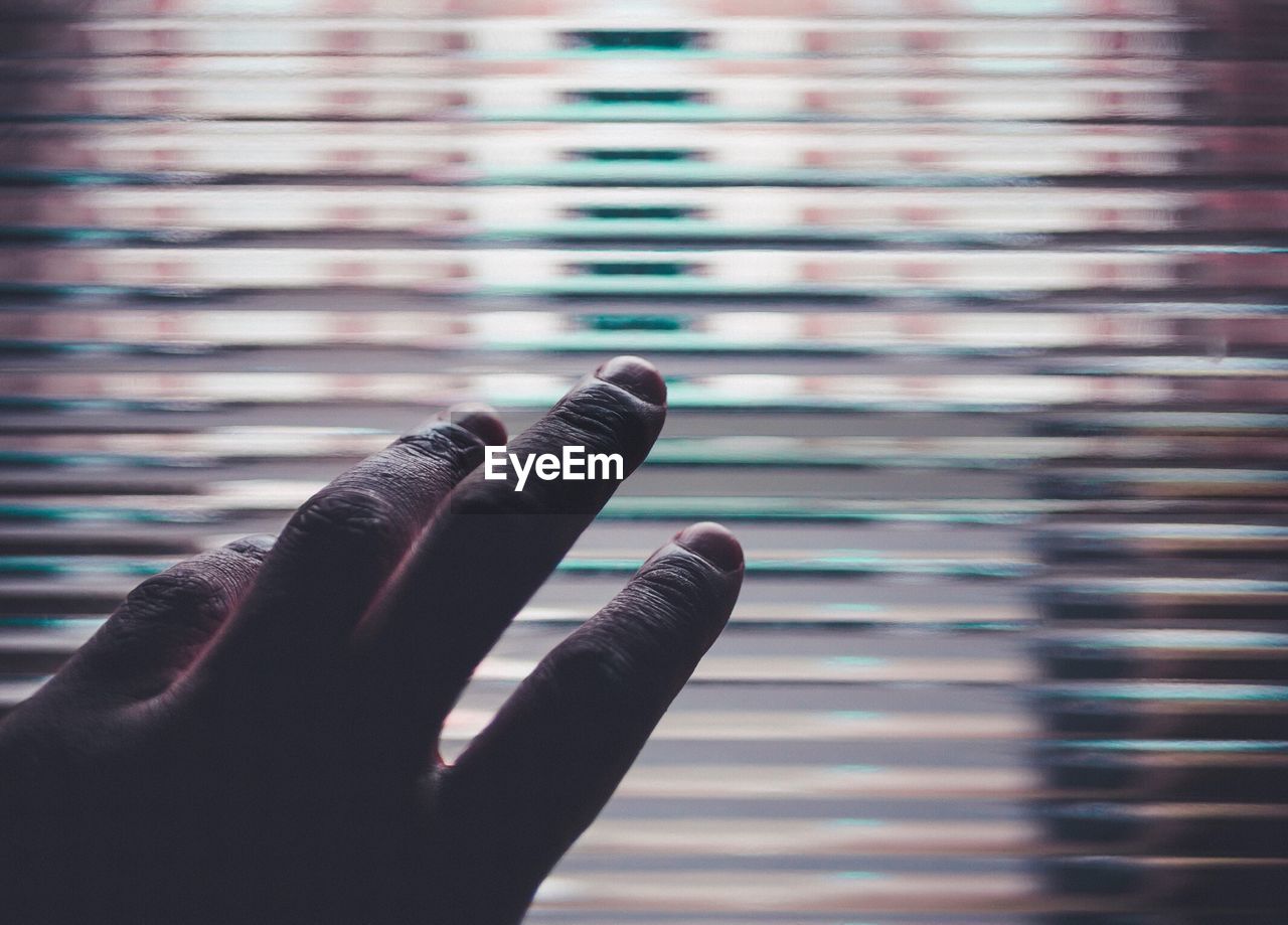 Cropped image of hand against window blinds