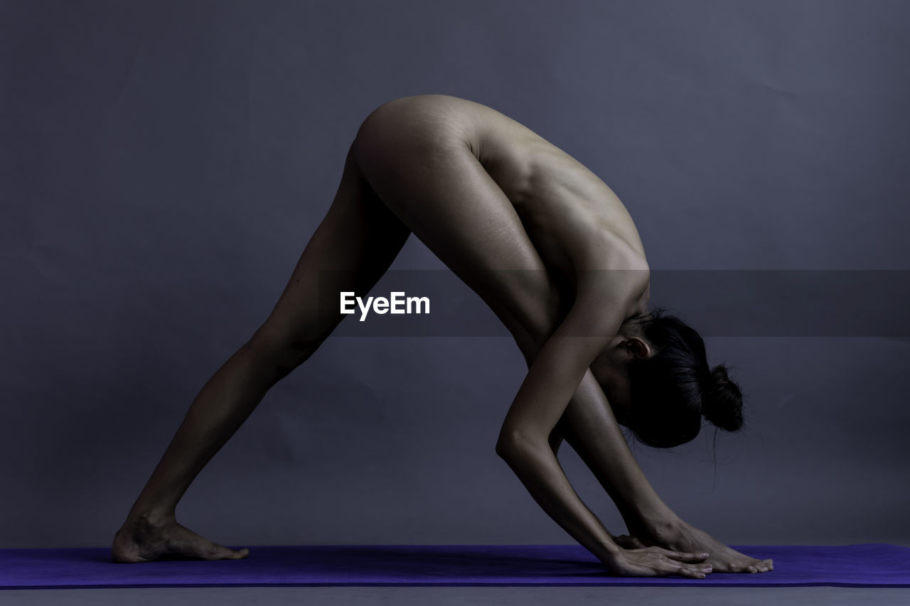 Full length of naked woman exercising against gray background