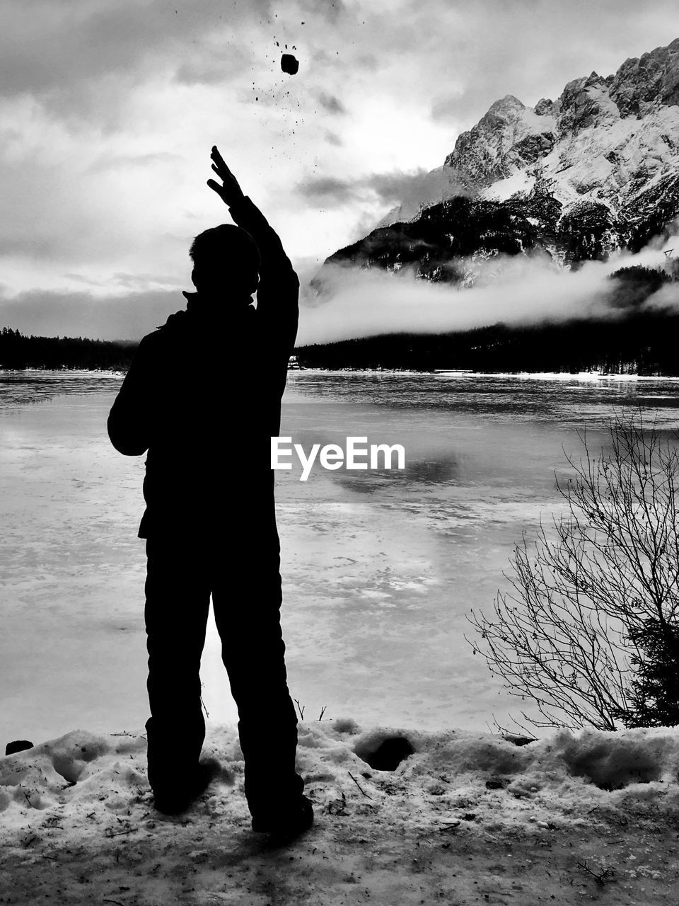 Man throwing stone in river against sky during winter