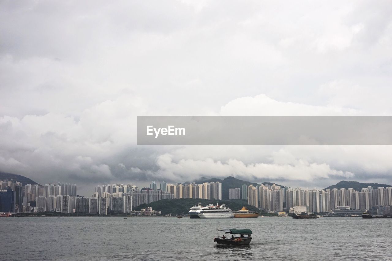 Scenic view of cityscape by sea against cloudy sky