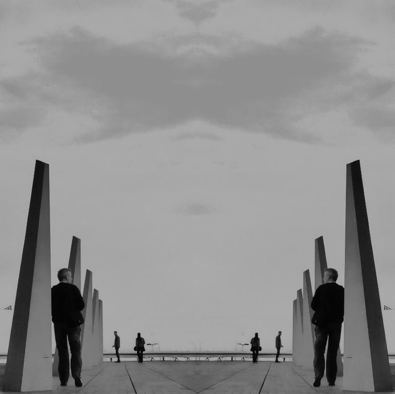 Mirror image of man by modern sculpture against sky