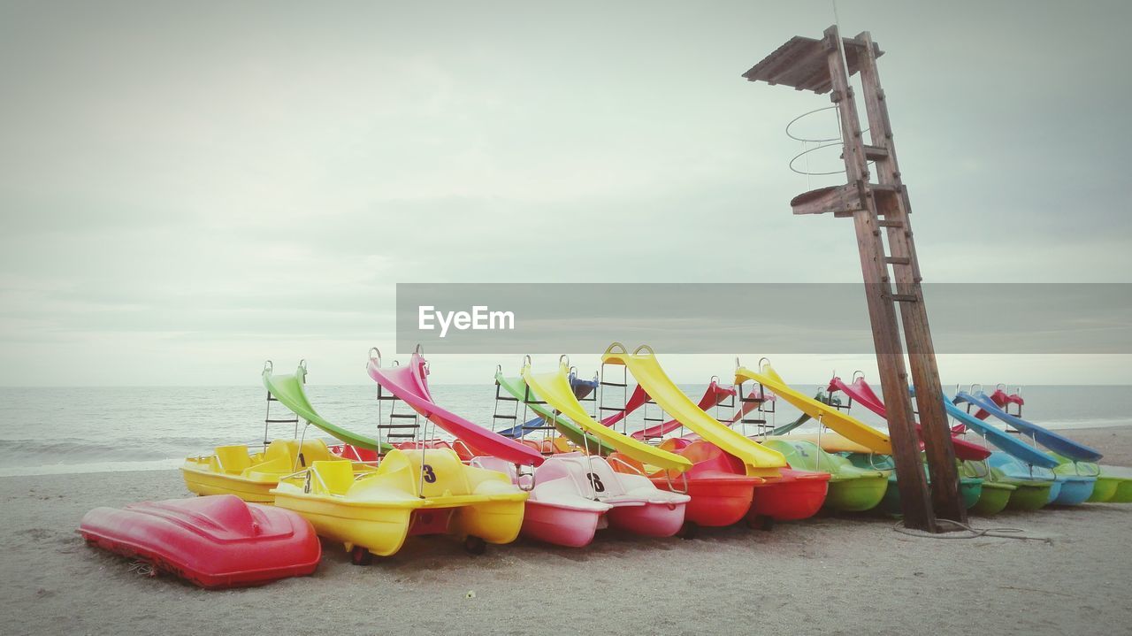 LOW ANGLE VIEW OF MULTI COLORED DECK CHAIRS ON BEACH AGAINST SKY