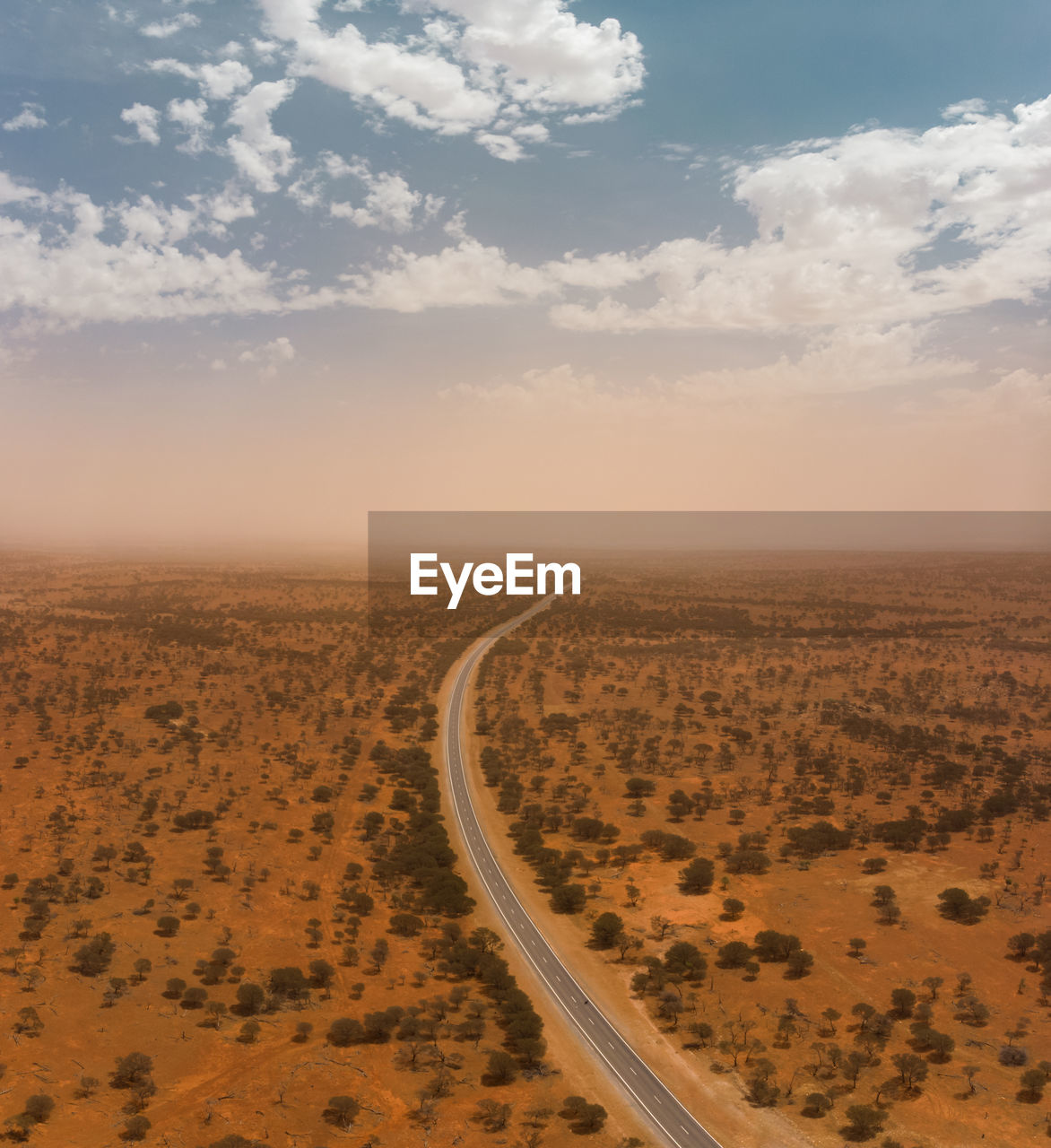 Drone aerial of a highway through the landscape of the outback with a massive dust storm on horizon