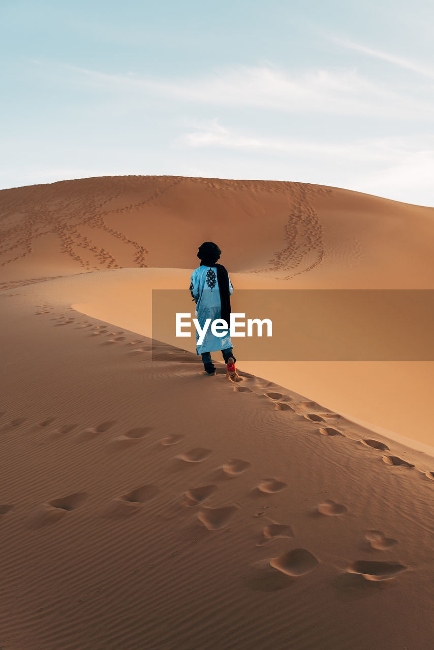 REAR VIEW OF MAN ON SAND DUNE IN DESERT