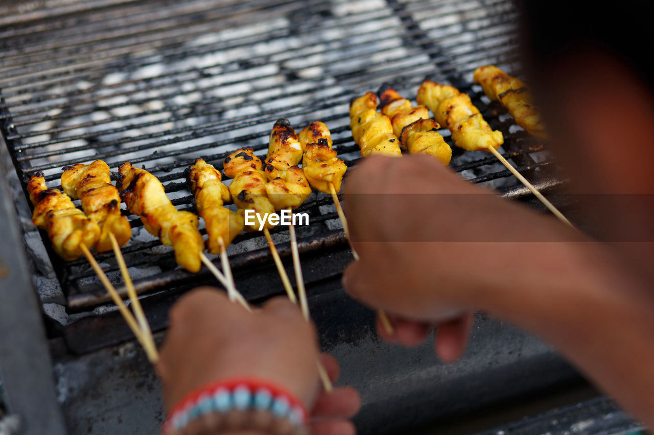 Cropped hands of person making satay on barbeque grill