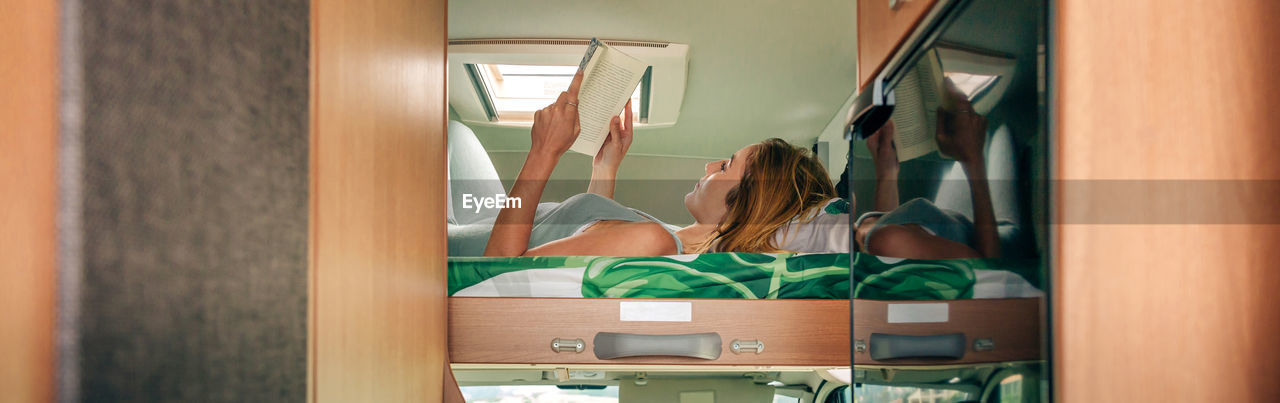 Woman reading book lying on camper van bunk bed