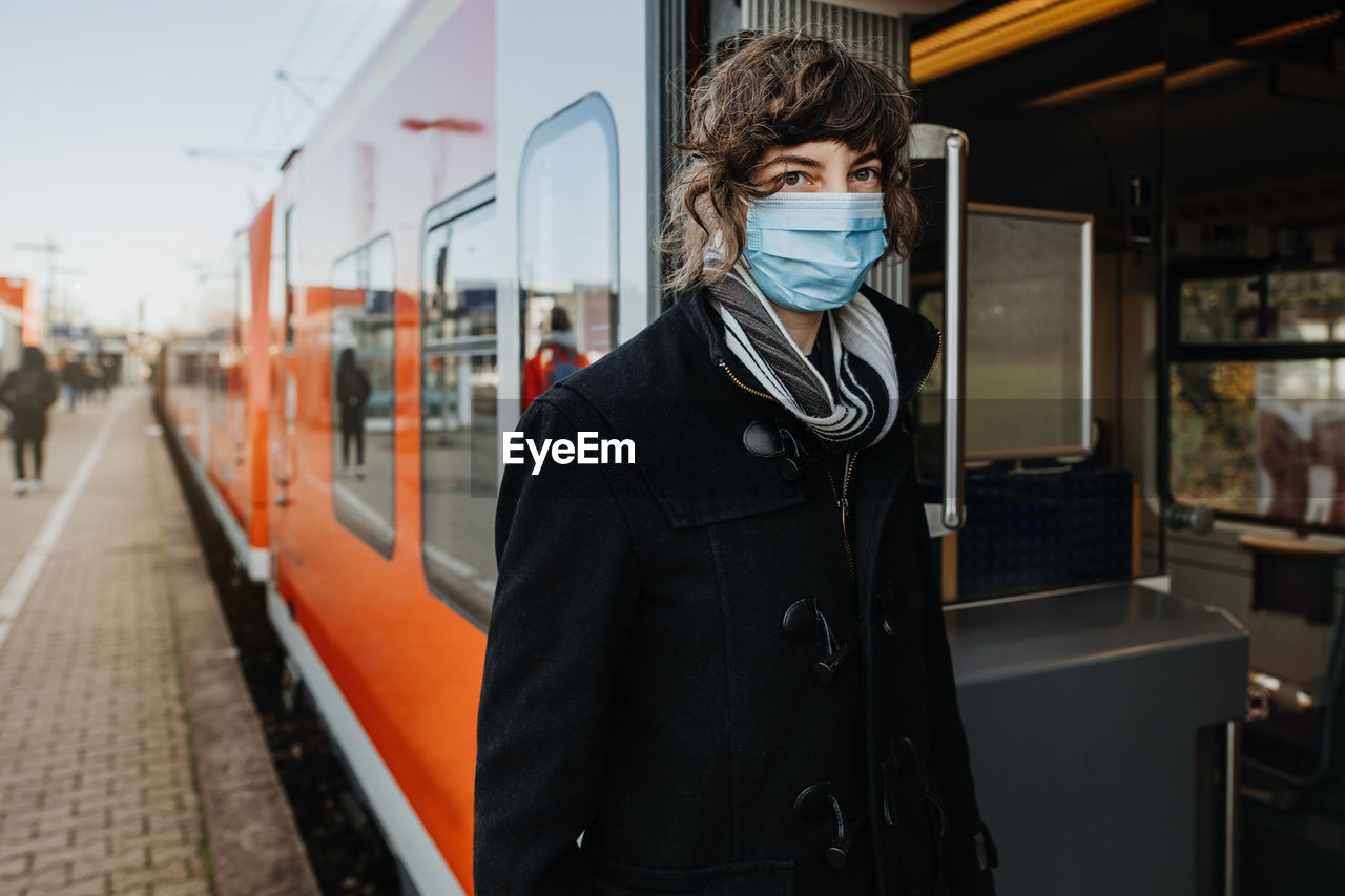 Portrait woman wearing mask standing by train on railroad station platform