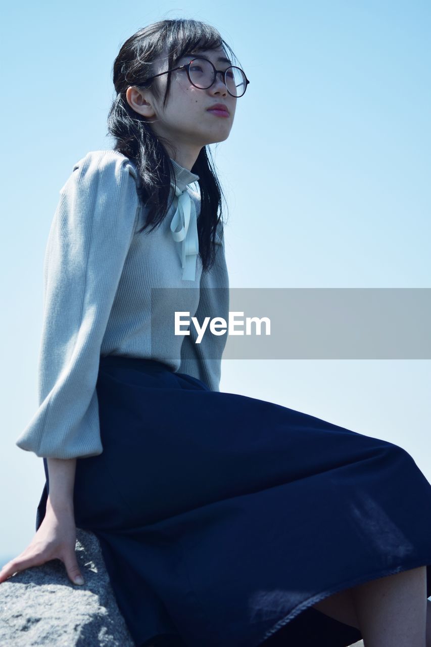 Young woman sitting on blue against sky