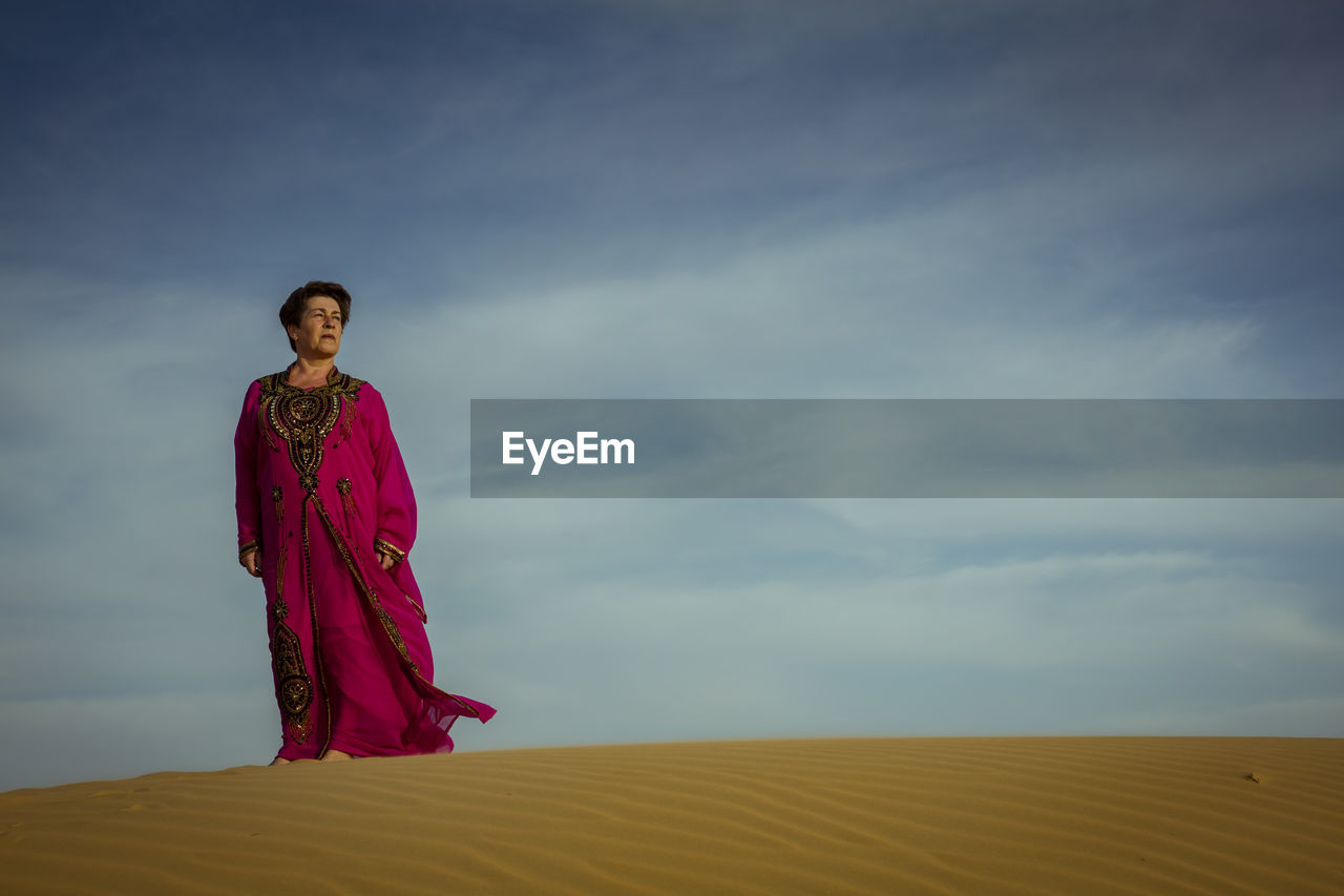 Low angle view of woman standing at desert against sky
