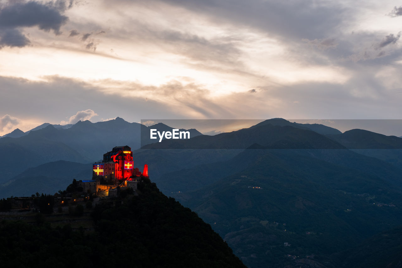 Scenic view of illuminated church on mountain range against sky during sunset