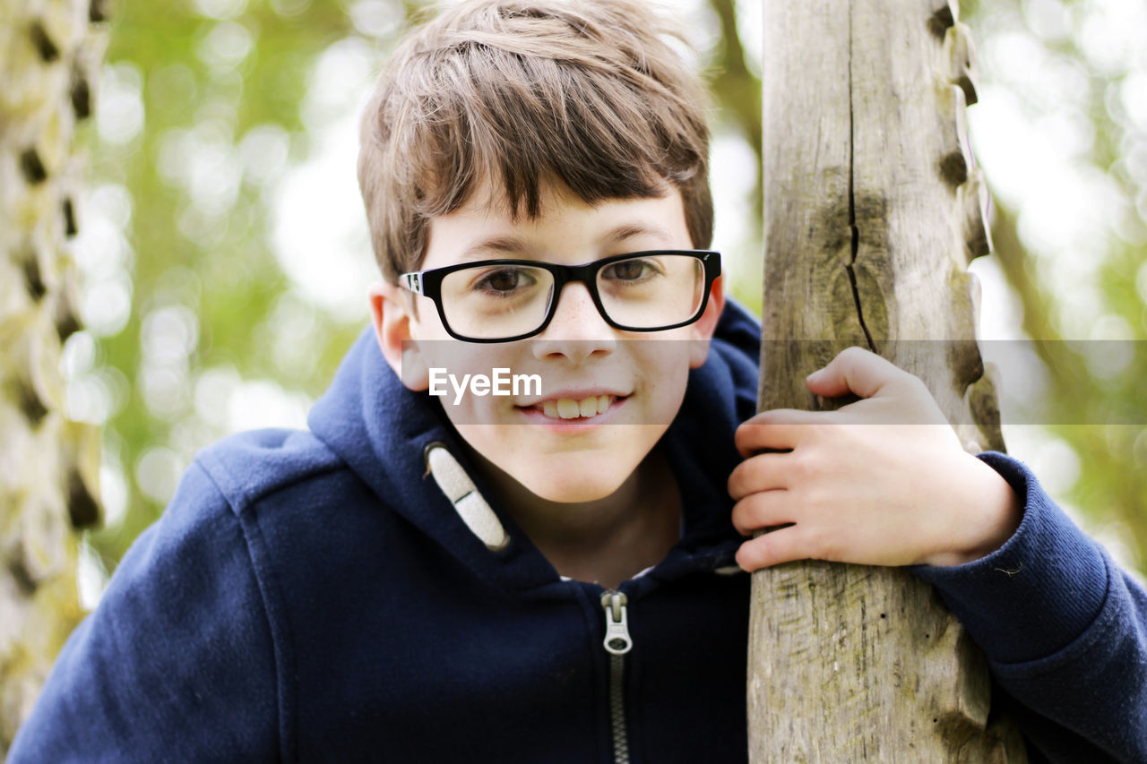 Portrait of boy wearing eyeglasses holding tree trunk