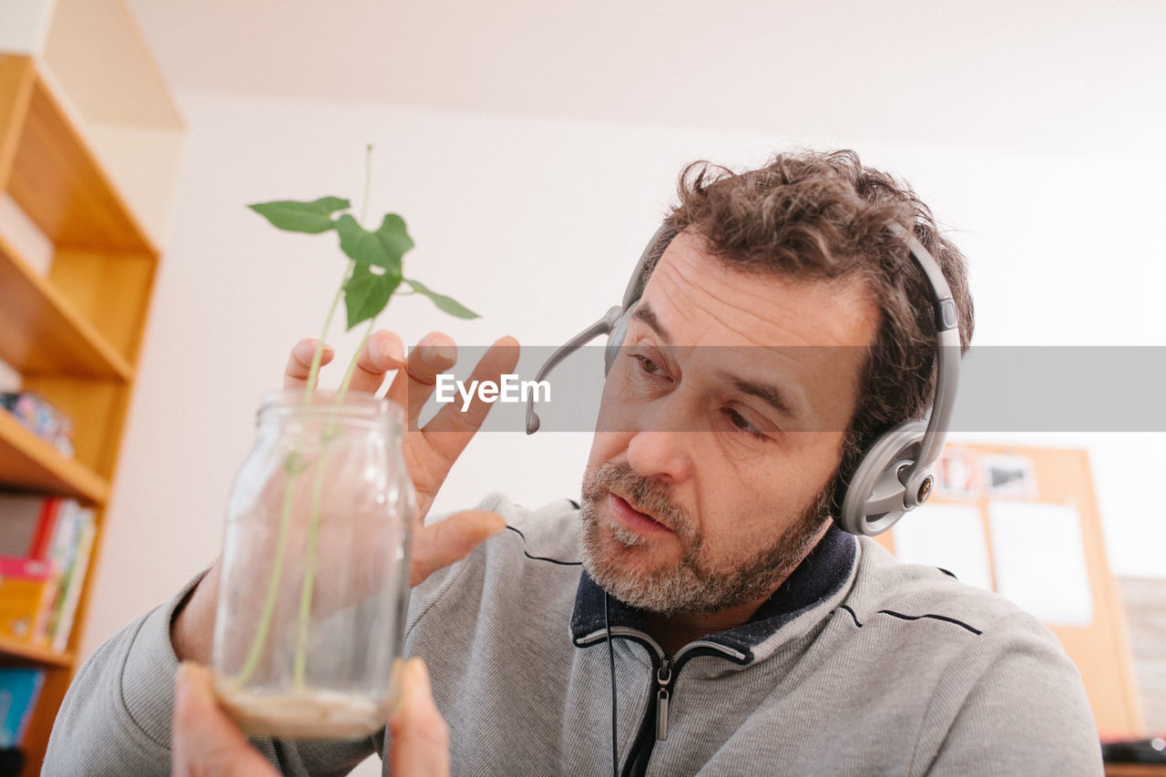Adult male teacher showing growth of plant in natural science project in home schooling video chat 