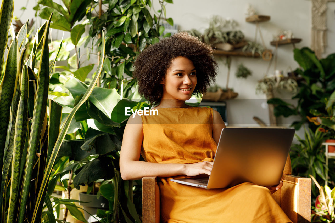 Teenage girl using laptop while sitting against plants