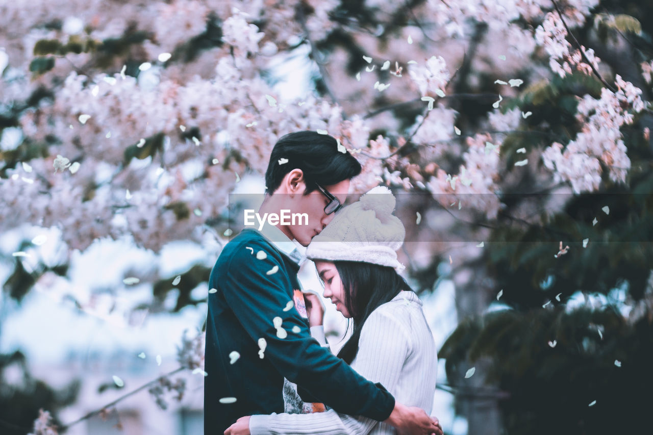 Side view of young couple embracing by flowering tree
