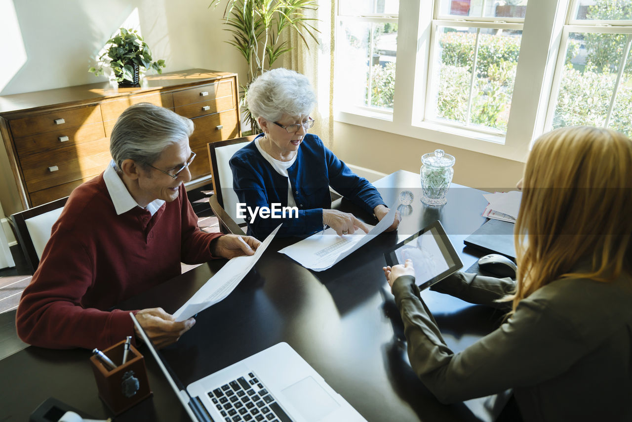 High angle view of senior couple reading documents while discussing with financial advisor in office