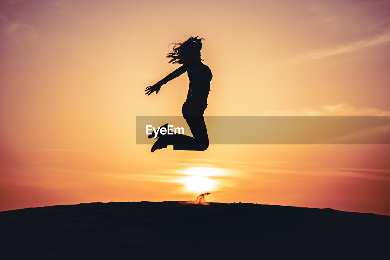 Silhouette woman jumping against orange sky during sunset