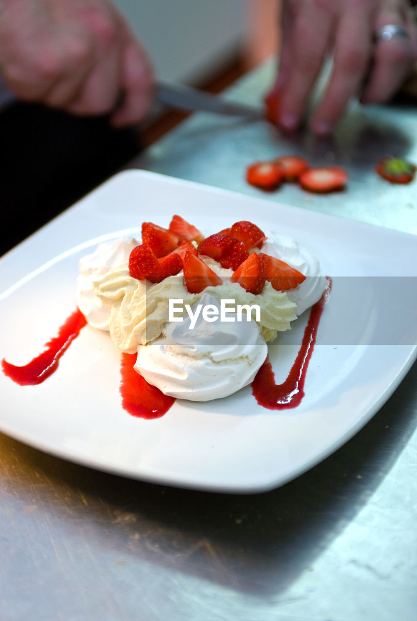 Chef preparing pavlova with fresh strawberries and cream