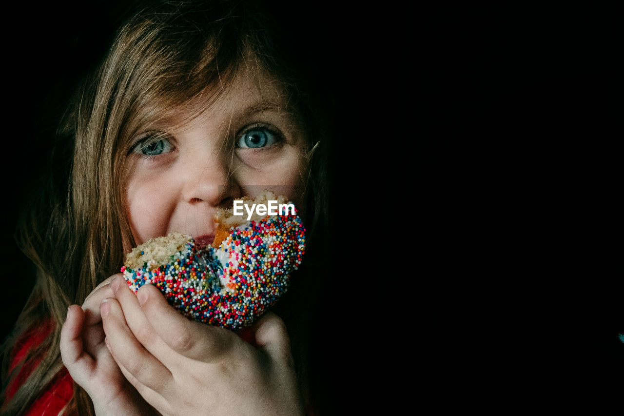 Portrait of girl eating donut against black background