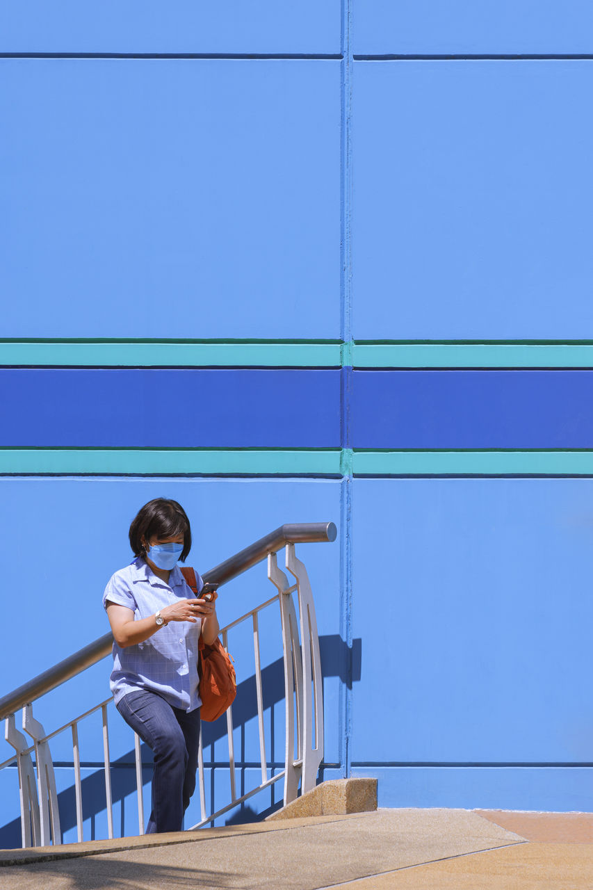 Asian woman using smartphone while walking up staircase outside of shopping mall