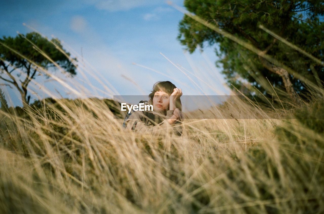Portrait of woman lying on field amidst grass against sky