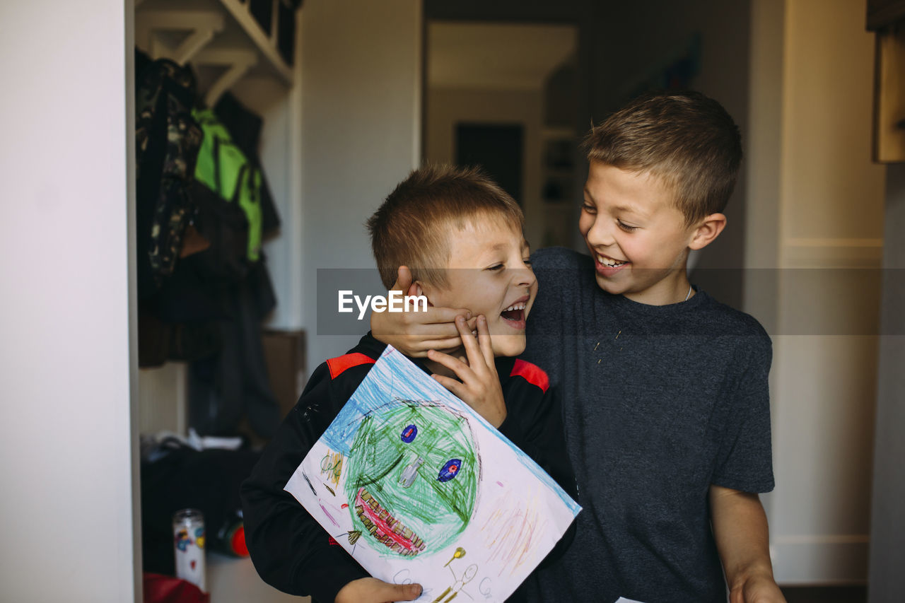 Cheerful boy holding brother's face while playing at home