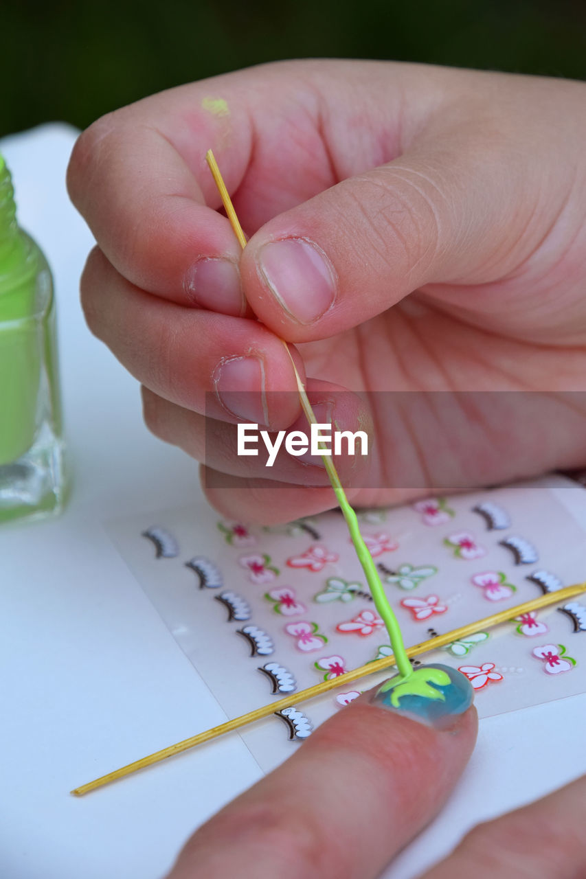 Cropped hand applying nail art on finger of woman