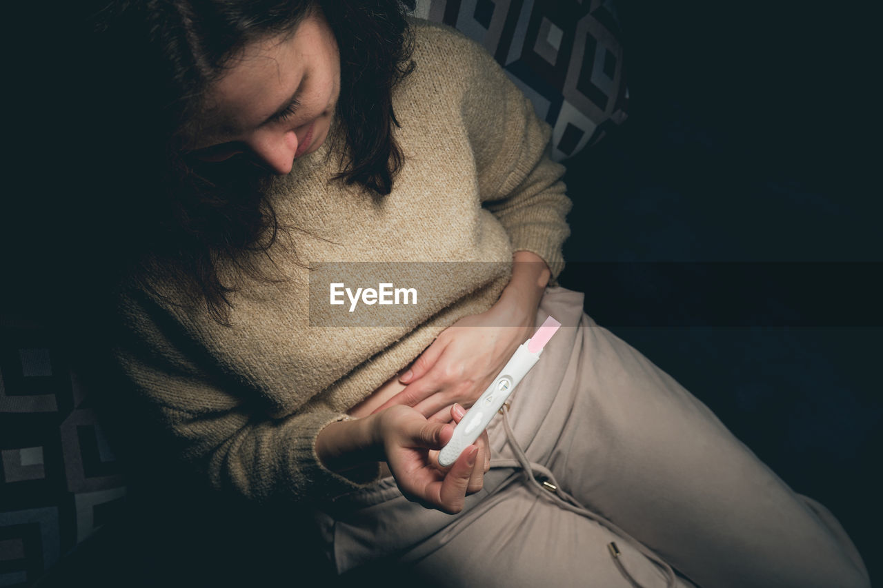 A woman in a dark room looks at the result of a pregnancy test and smiles